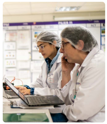 Two people working next to each other on laptops, wearing protective lab gear.