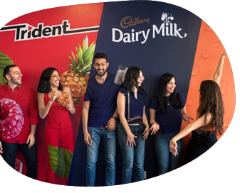 A group of smiling people standing in front of a wall with "Trident" and "Cadbury Dairy Milk" signs.