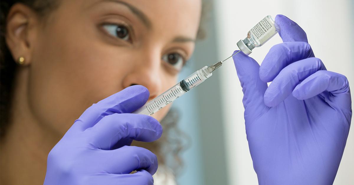 A person wearing protective gloves drawing a vaccine from a vial with a needle.