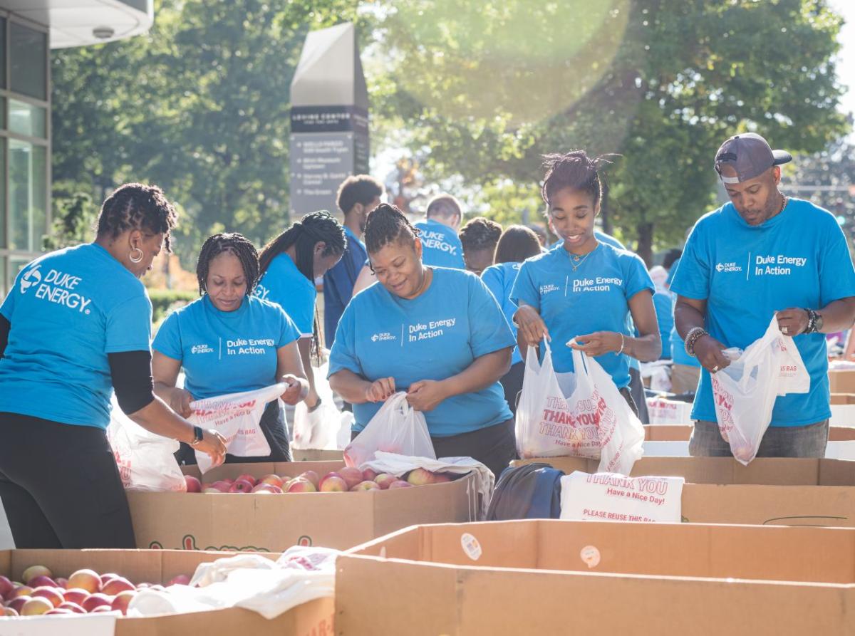 Volunteers packing bags with produce items in large bins outside.