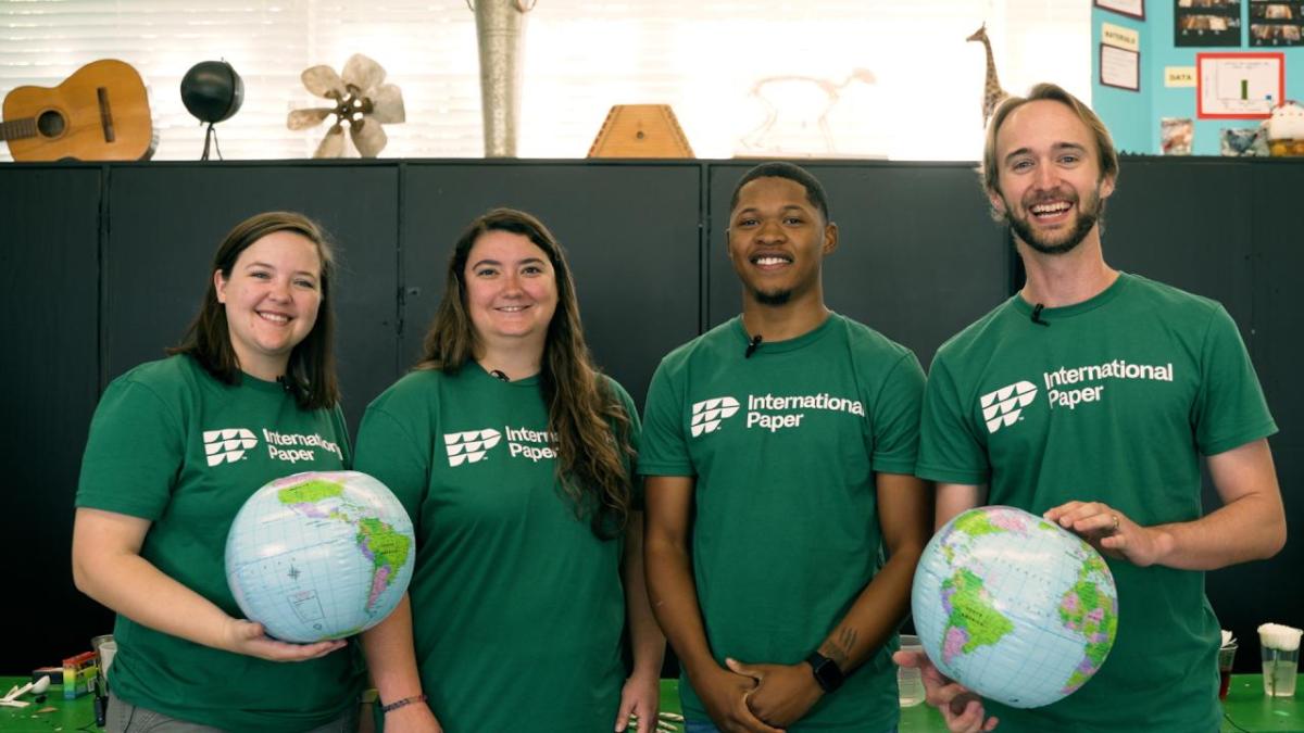 four people stood next to each other wearing green t-shirts, with the people either side holding a globe
