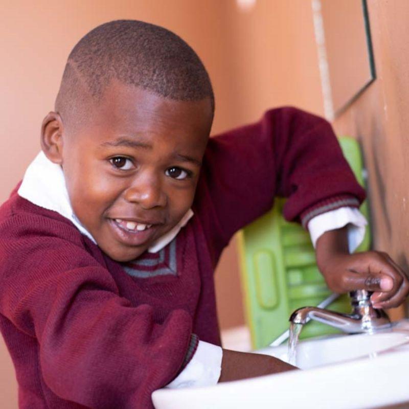 A smiling child washing their hands in a sink.