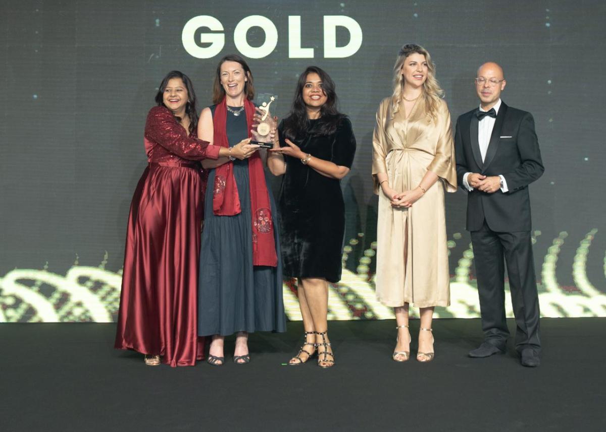 Five people on a stage in front of the word "GOLD", three holding an award