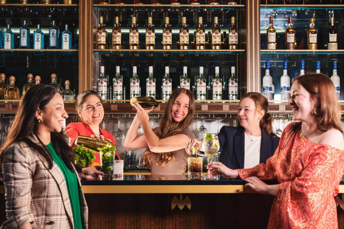 Five women posed in a bar setting with bottles on shelves behind them.