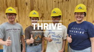 Four people giving thumbs-up, wearing matching yellow hard hats. "Thrive" on top of the image.