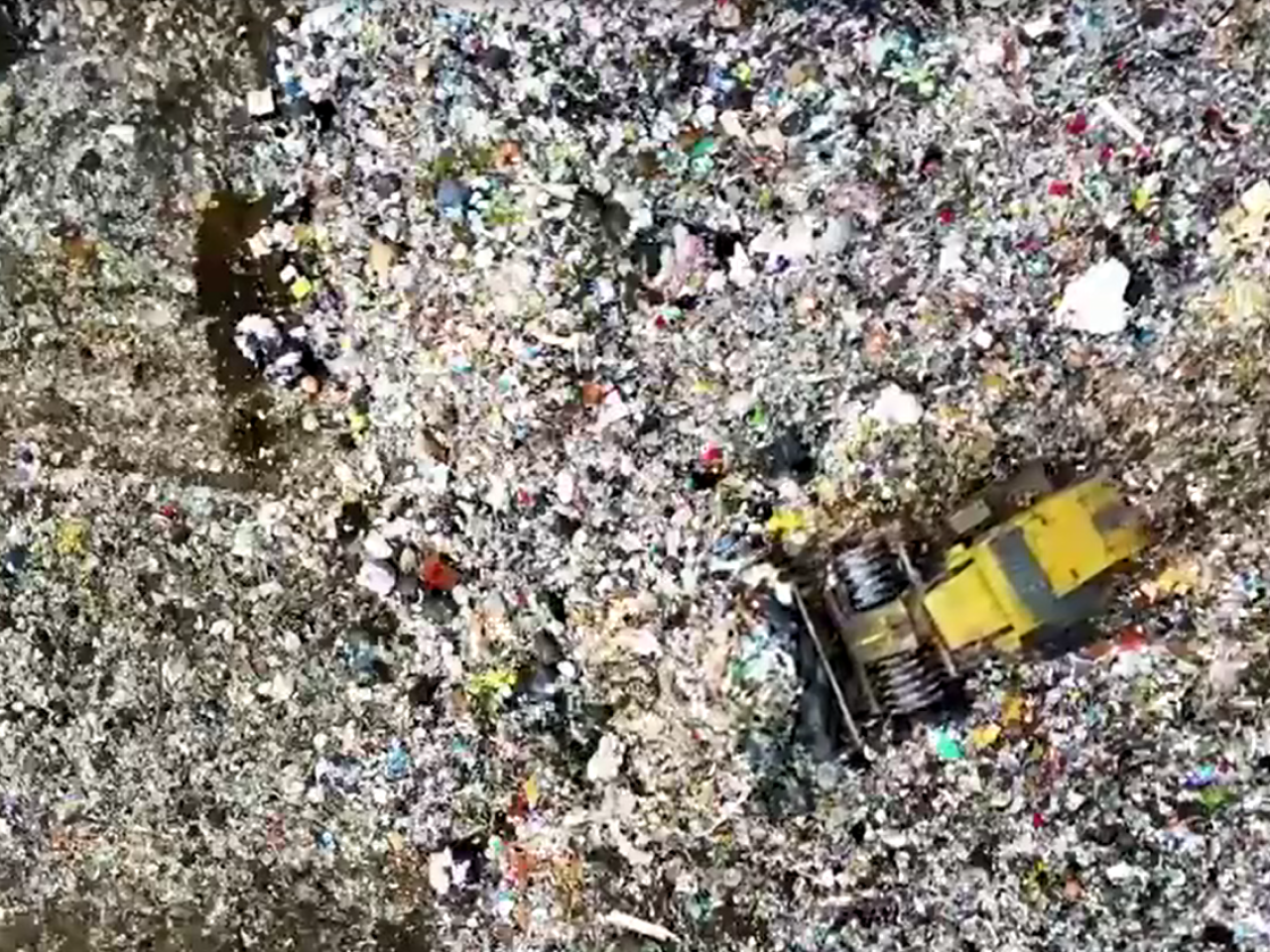 A bulldozer pushing piles of garbage in a dump.