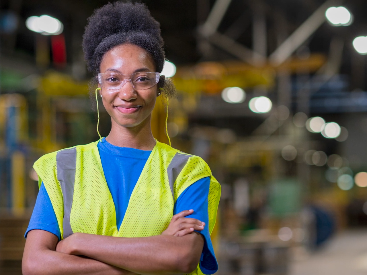 Person smiling with their arms folded, wearing safety glasses and a hi-vis vest