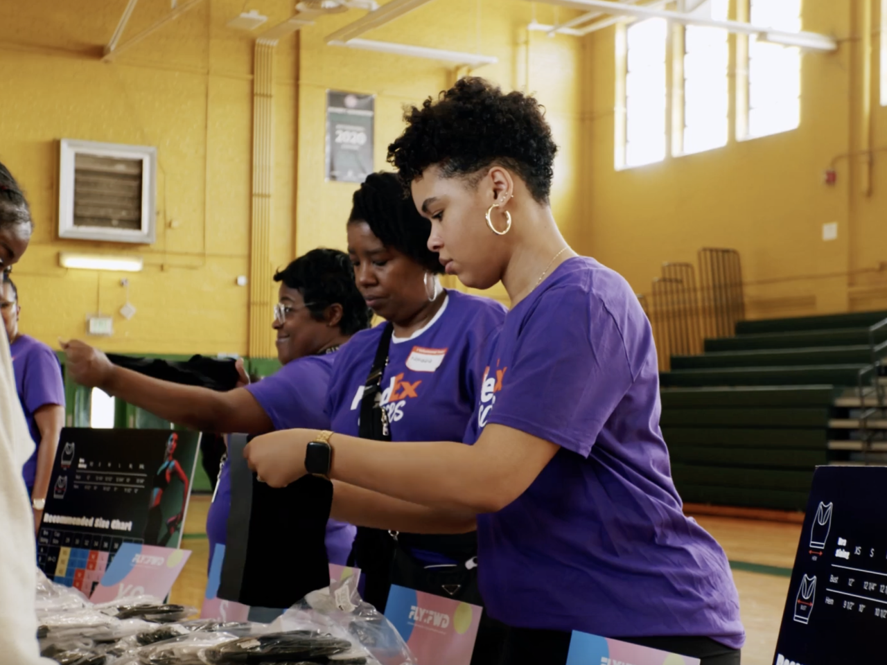 Girls wearing FedEx shirts at a table inside a gym