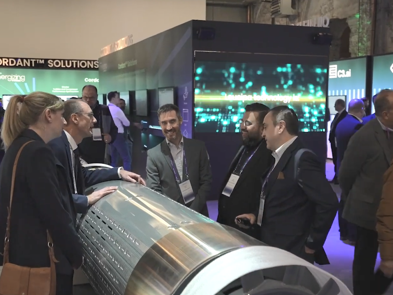 People talking over a large metal cylinder at a convention.