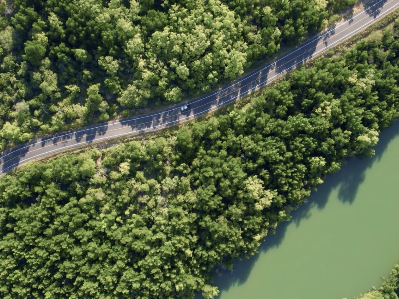 Birds eye view of a road surrounded by trees next to water