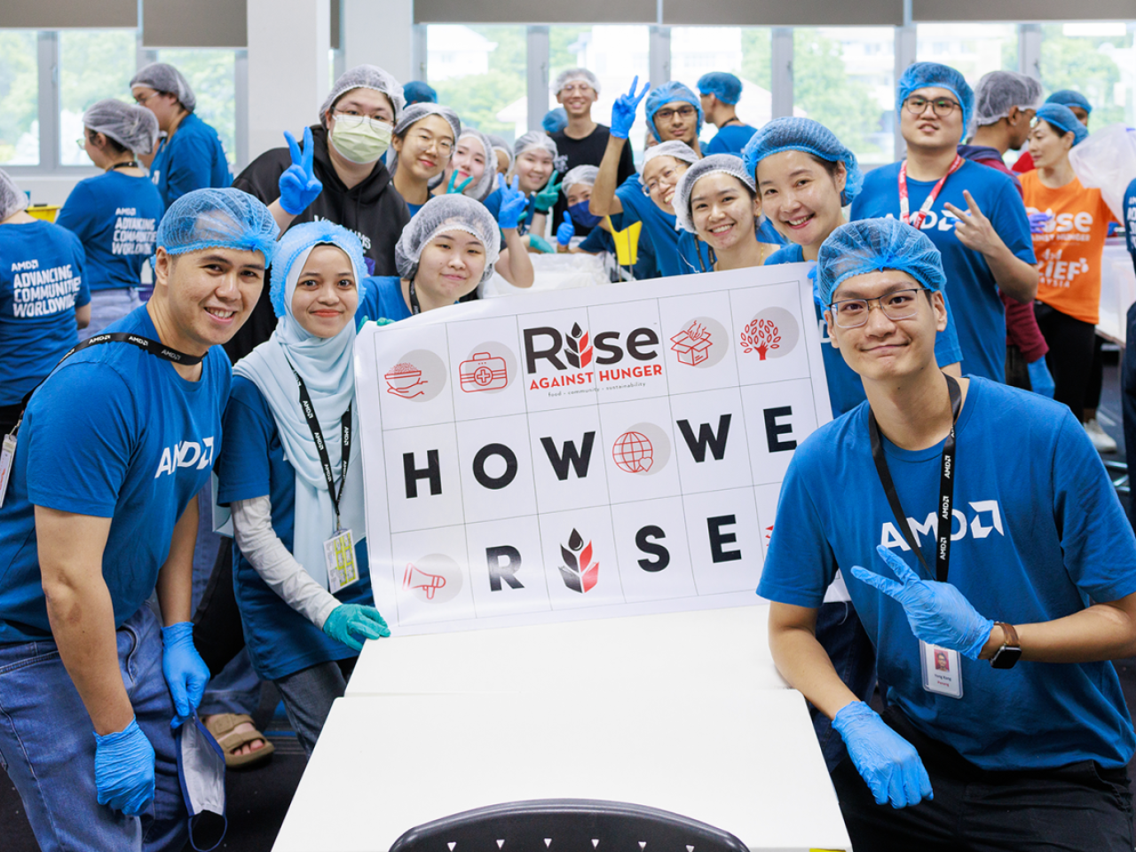 People in AMD t-shirts, gloves and hair nets posing for the camera with a sign that says: "How We Rise"