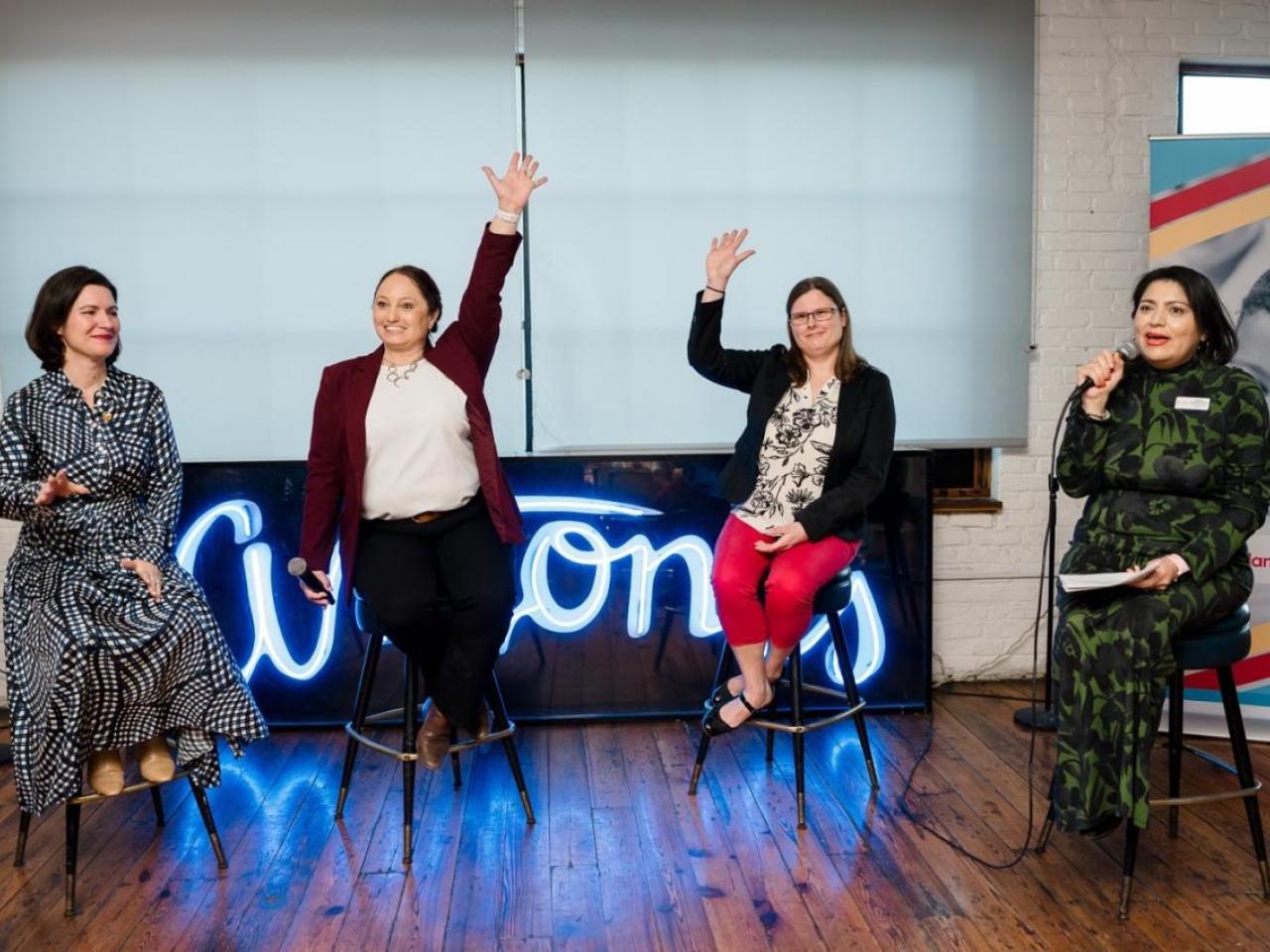 A group of women sitting on stools with their hands up