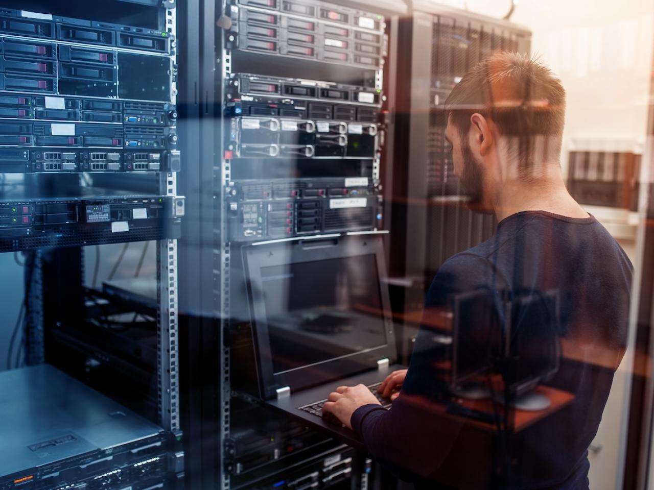 A person with a laptop working in a server room.