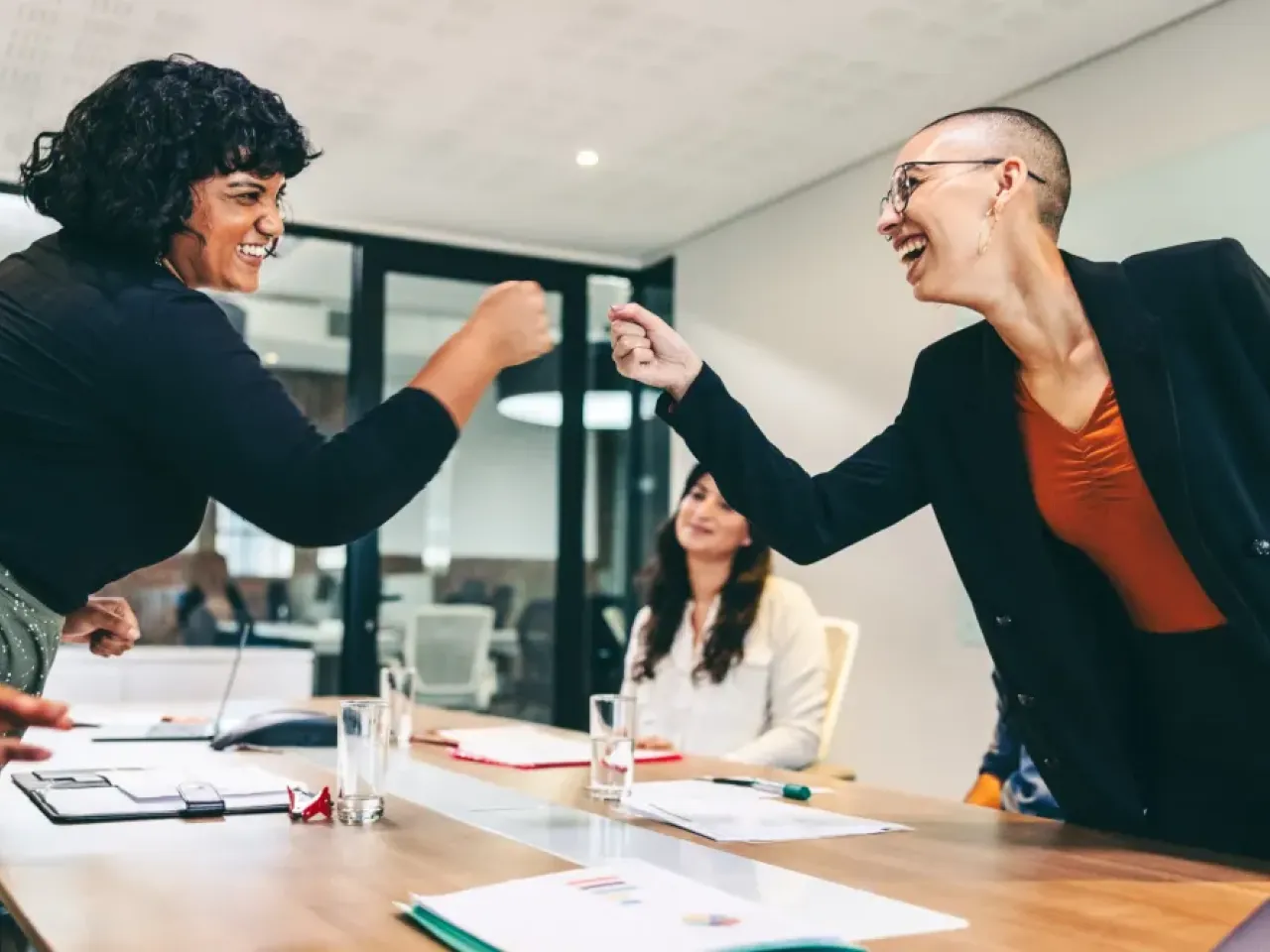 Two diverse colleagues smile and fist bump during a meeting, symbolizing support, inclusion, and positive workplace culture.