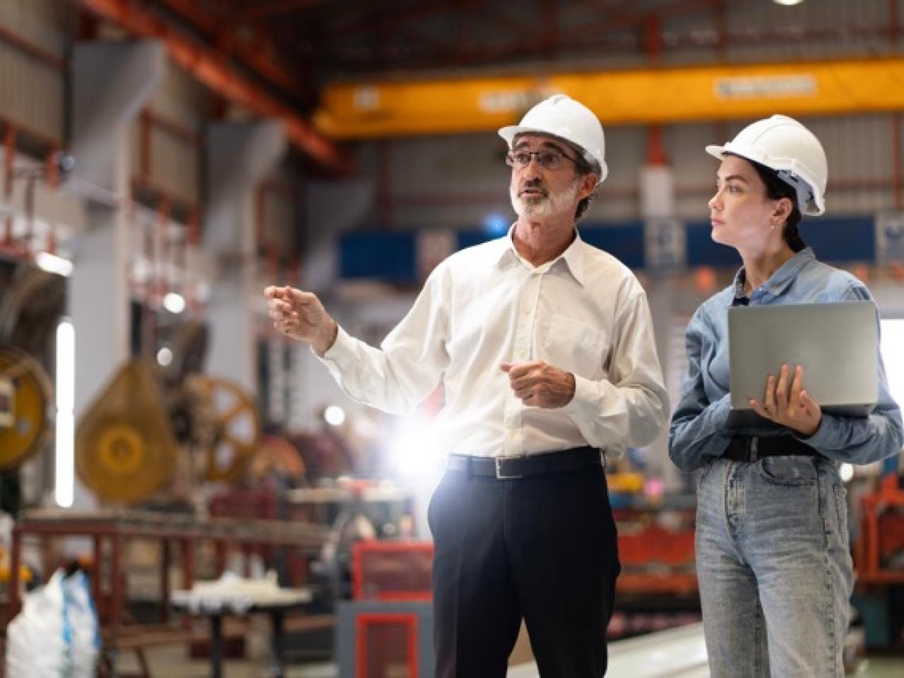 Two people wearing hard hats speaking in a workshop