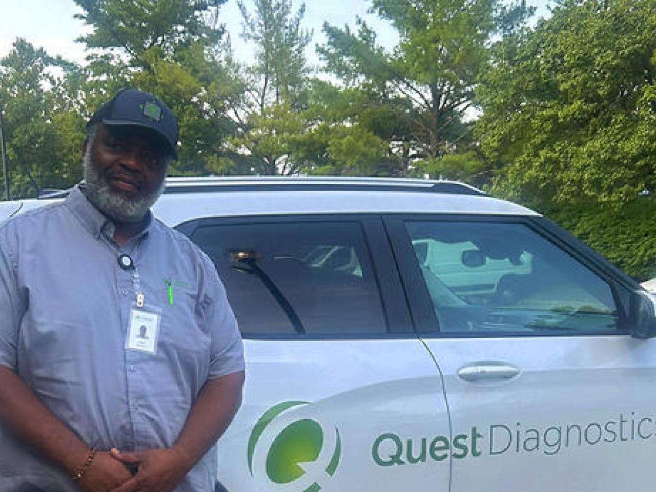 A person leaning against a white car that has the Quest Diagnostics logo on the side