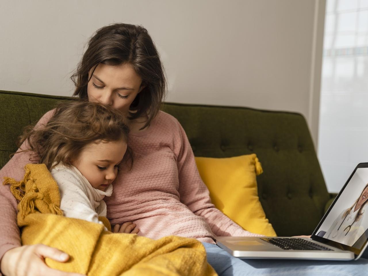 Mom and daughter seated on a couch together.