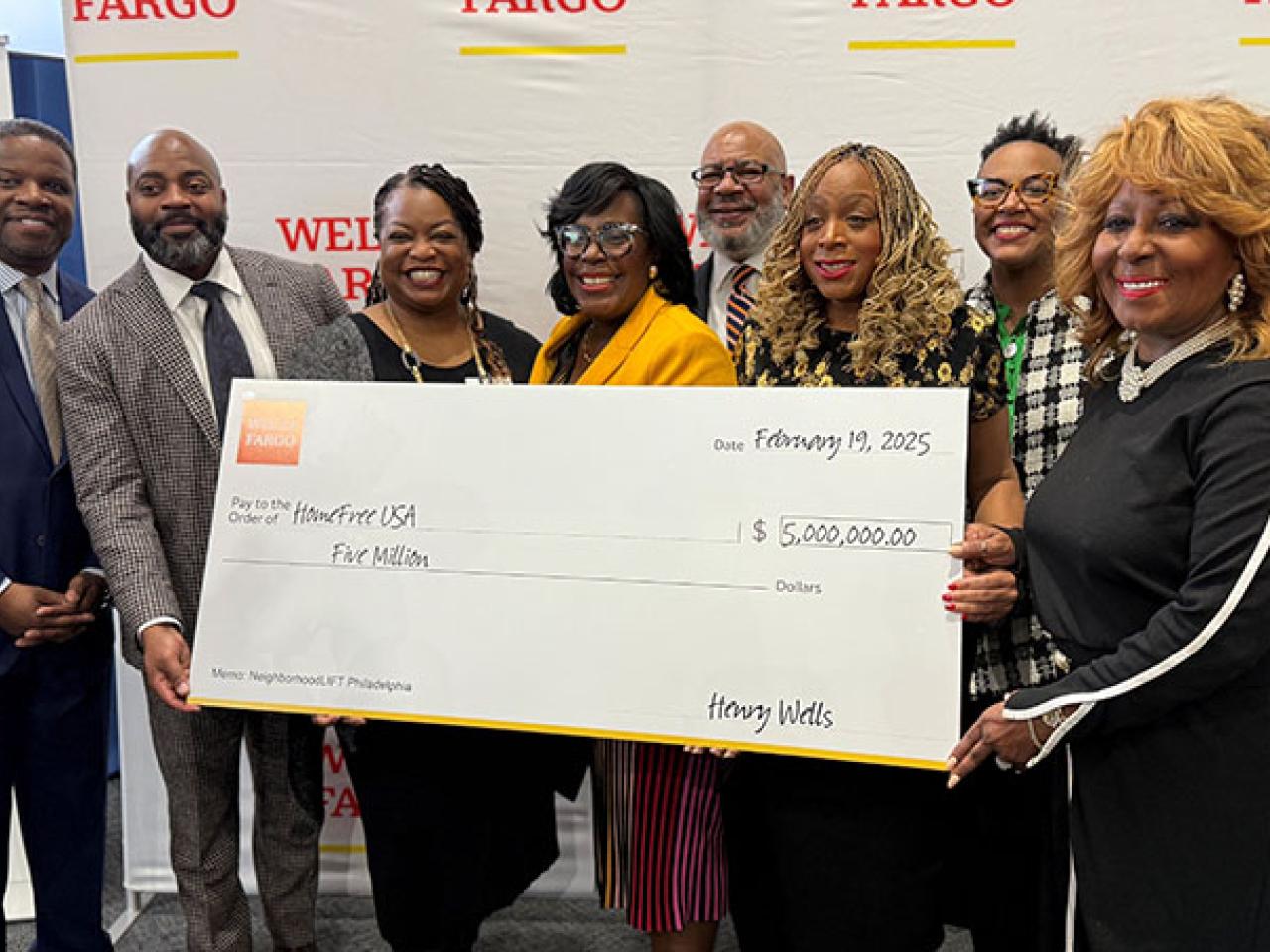 Group of people standing in front of a conference room holding a $5 million check.