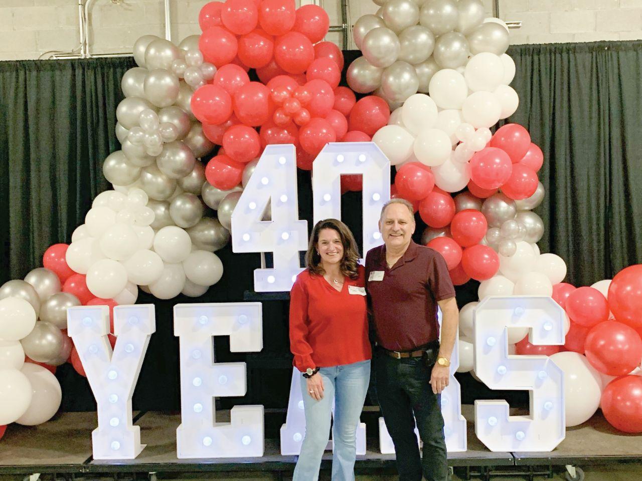 Two people standing in front of balloon display and sign reading "40 Years"