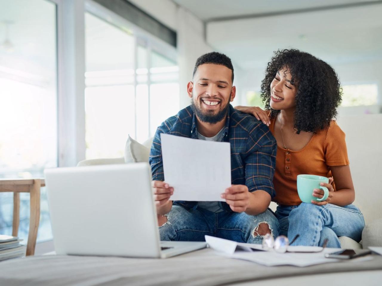 Smiling couple sitting on couch and looking at a piece of paper together