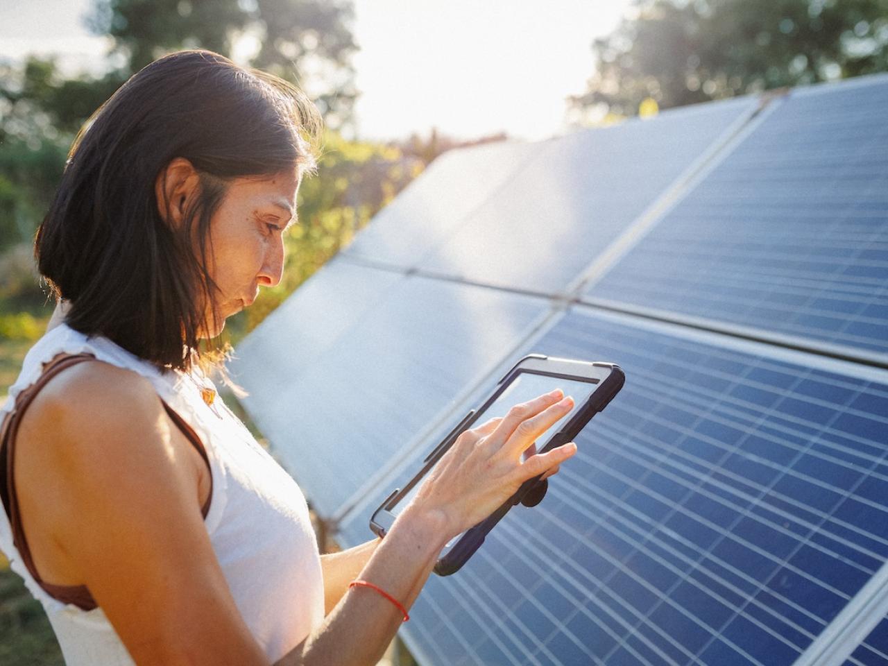 Woman holding a tablet and standing in front of a solar panel array.