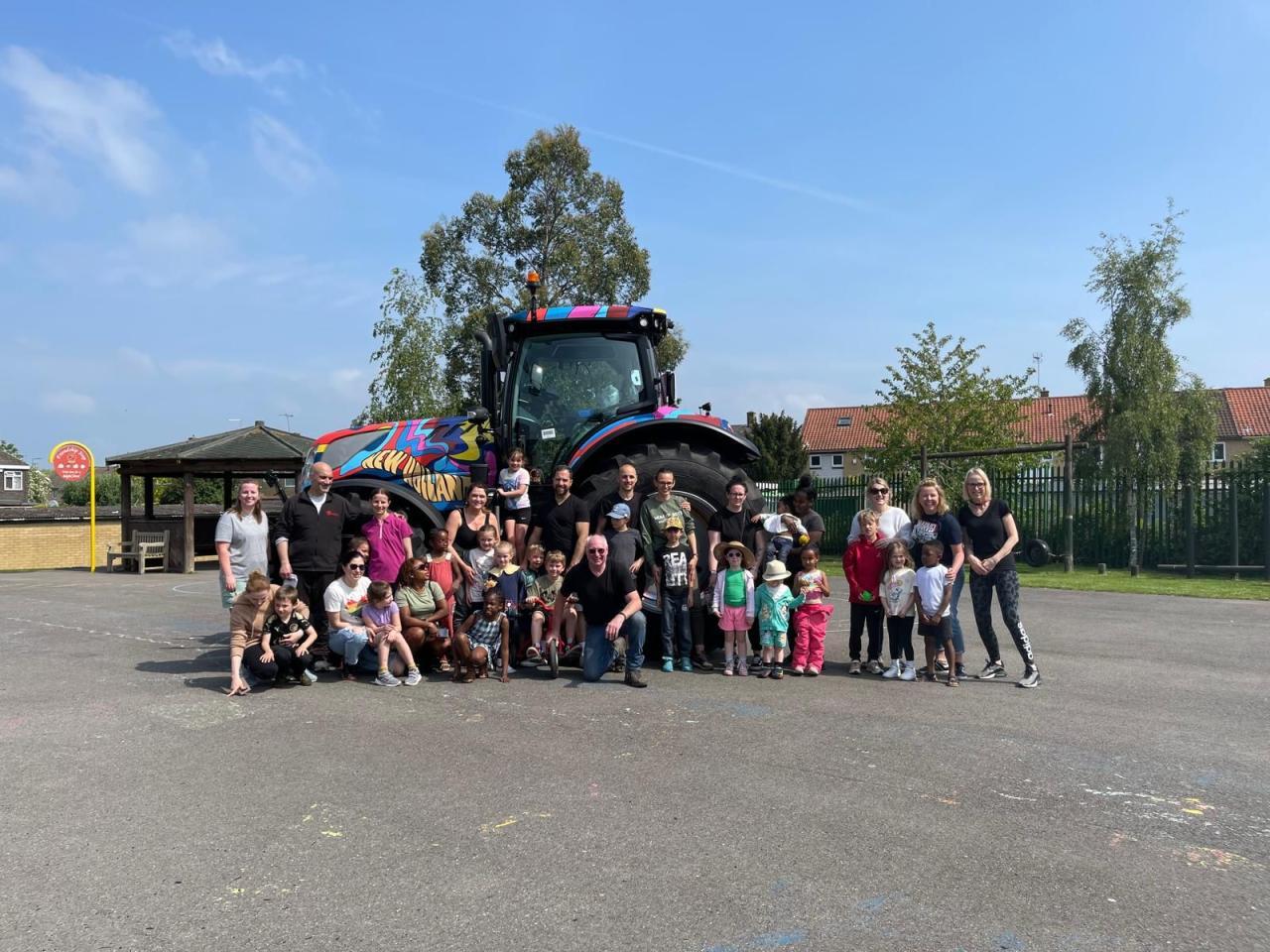 A large group of children and adults stood together in front of a colourful tractor