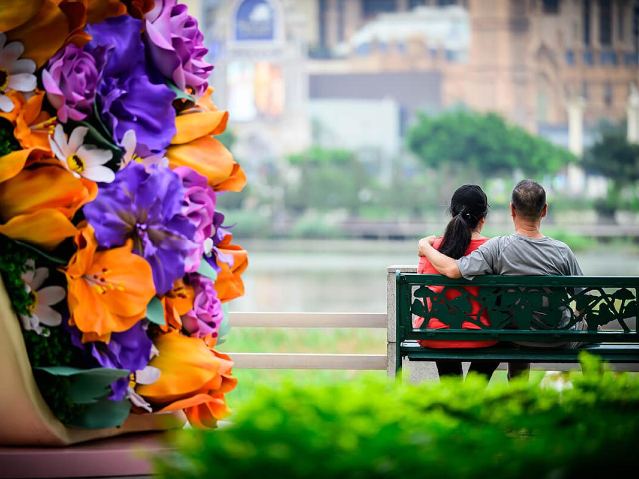 2 people sitting on a bench in front of flowers