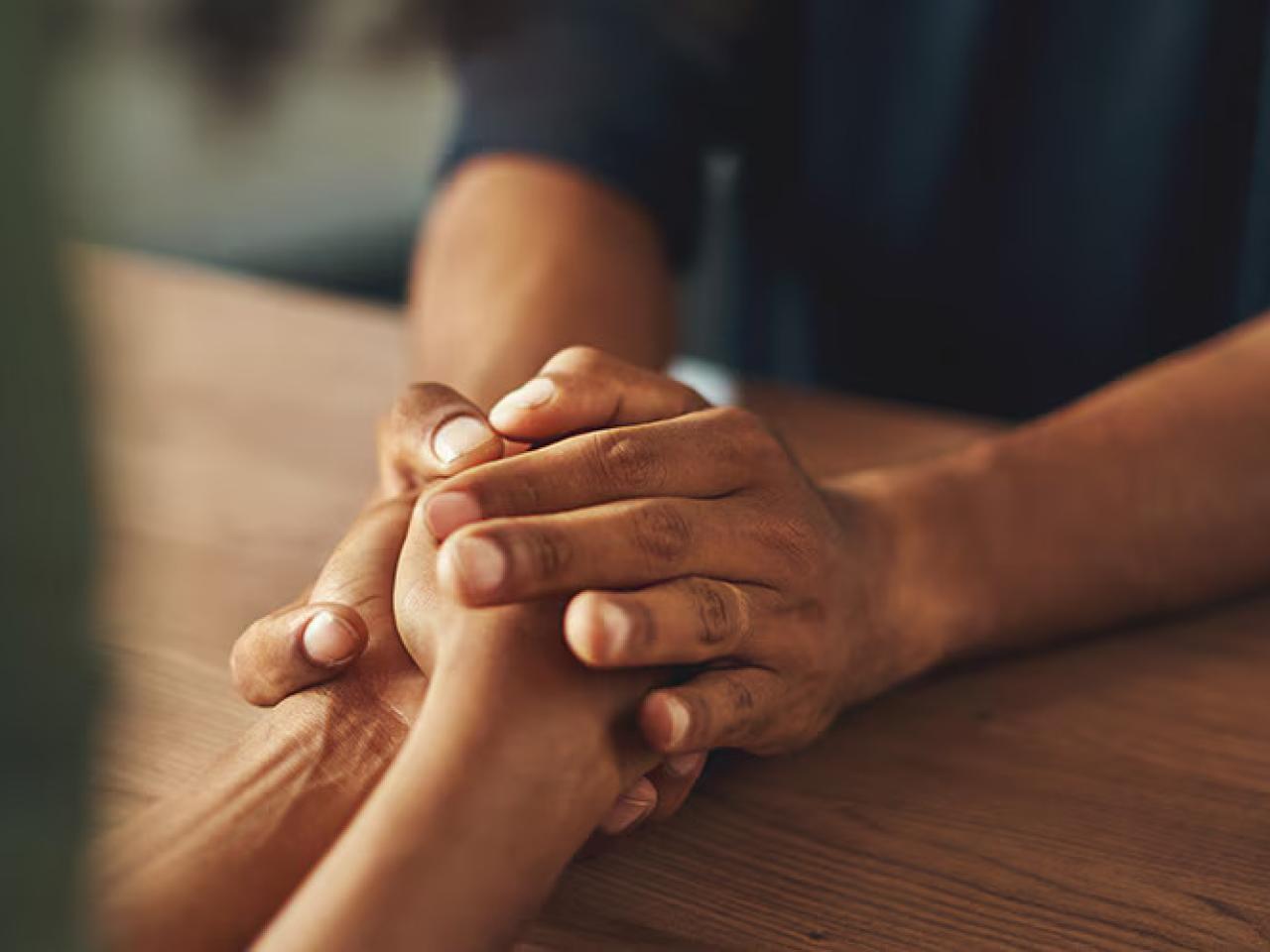 Close up of two people holding hands over a table.