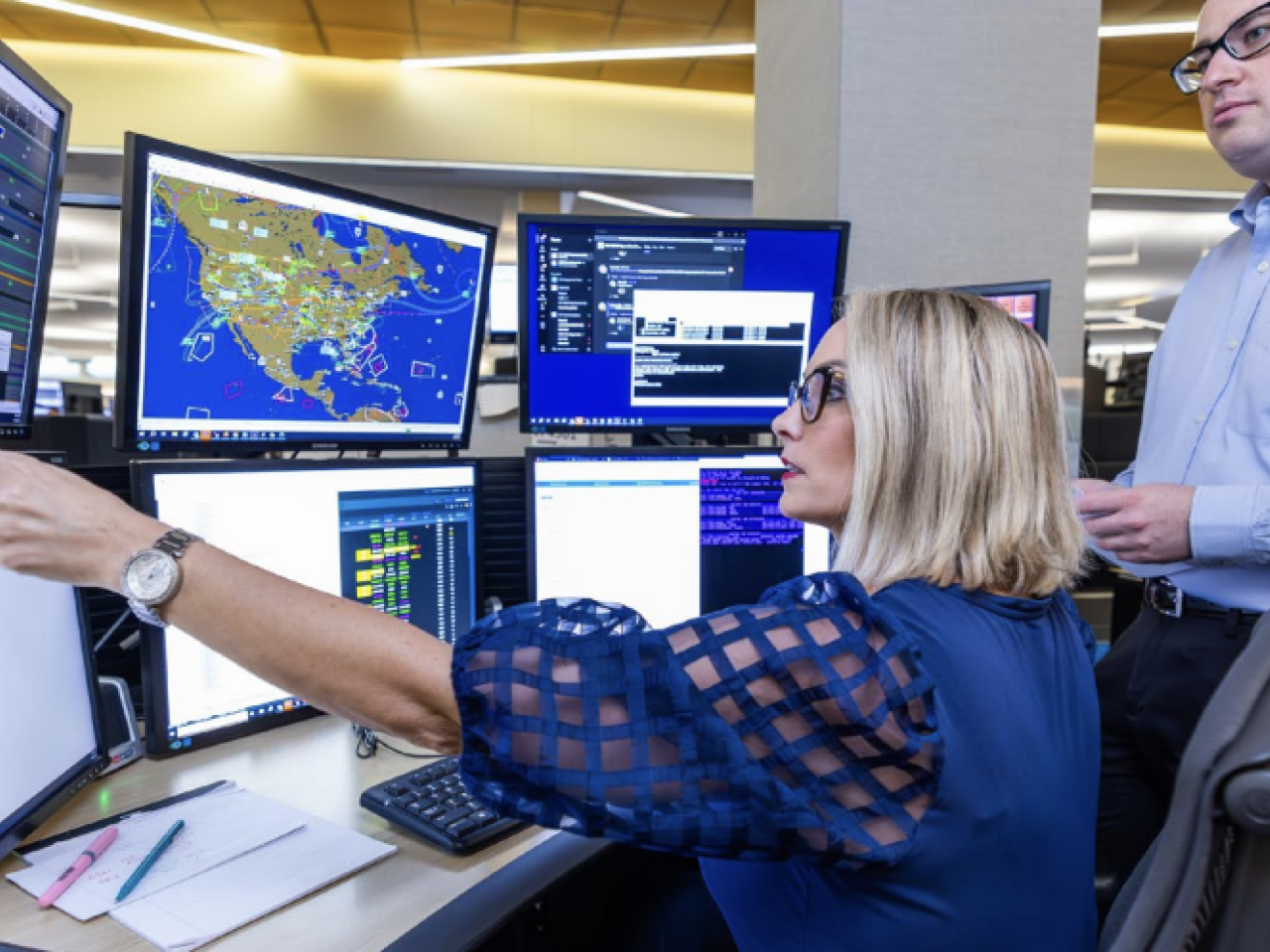 Two people looking at multiple computer monitors 