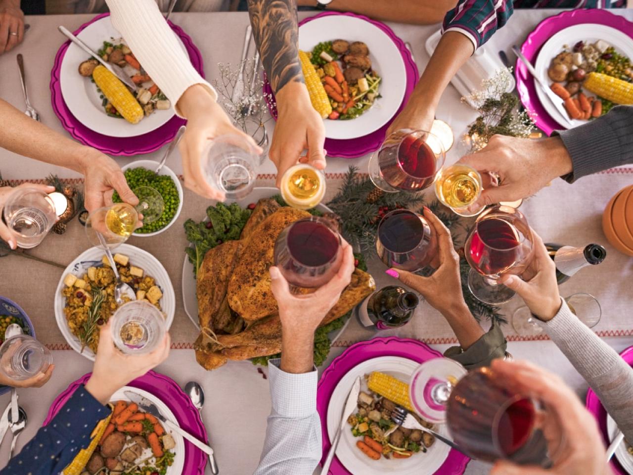 Many hands, each holding a beverage glass, meeting at the center of a table full of different foods.