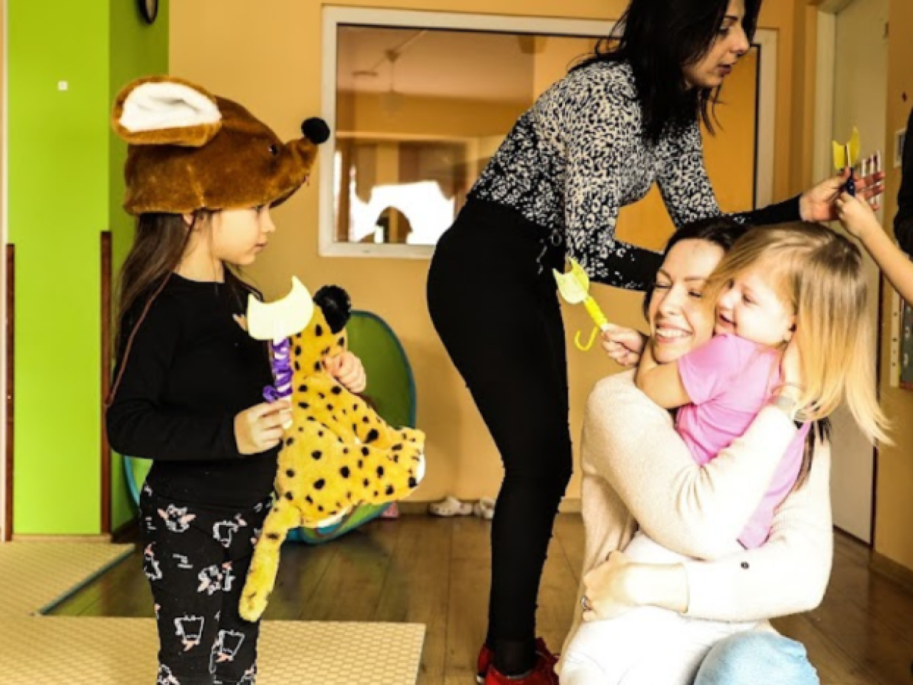 Children and adults smiling and gathering together in a lime green room, one child has a stuffed tiger.