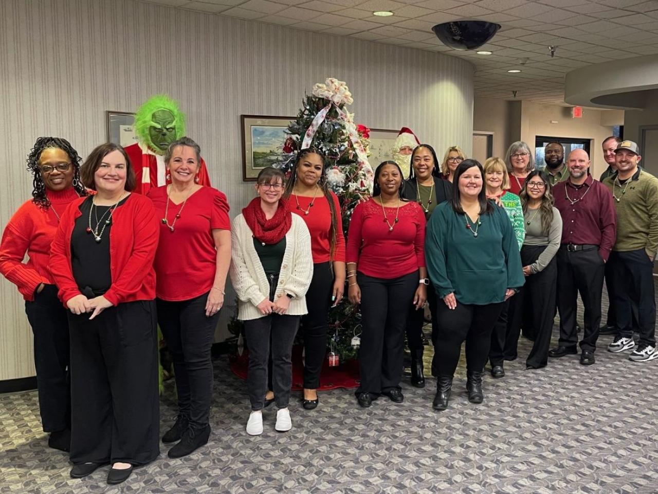 A group of volunteers posed in front of a chistmas tree. One dressed as the grinch behind them.