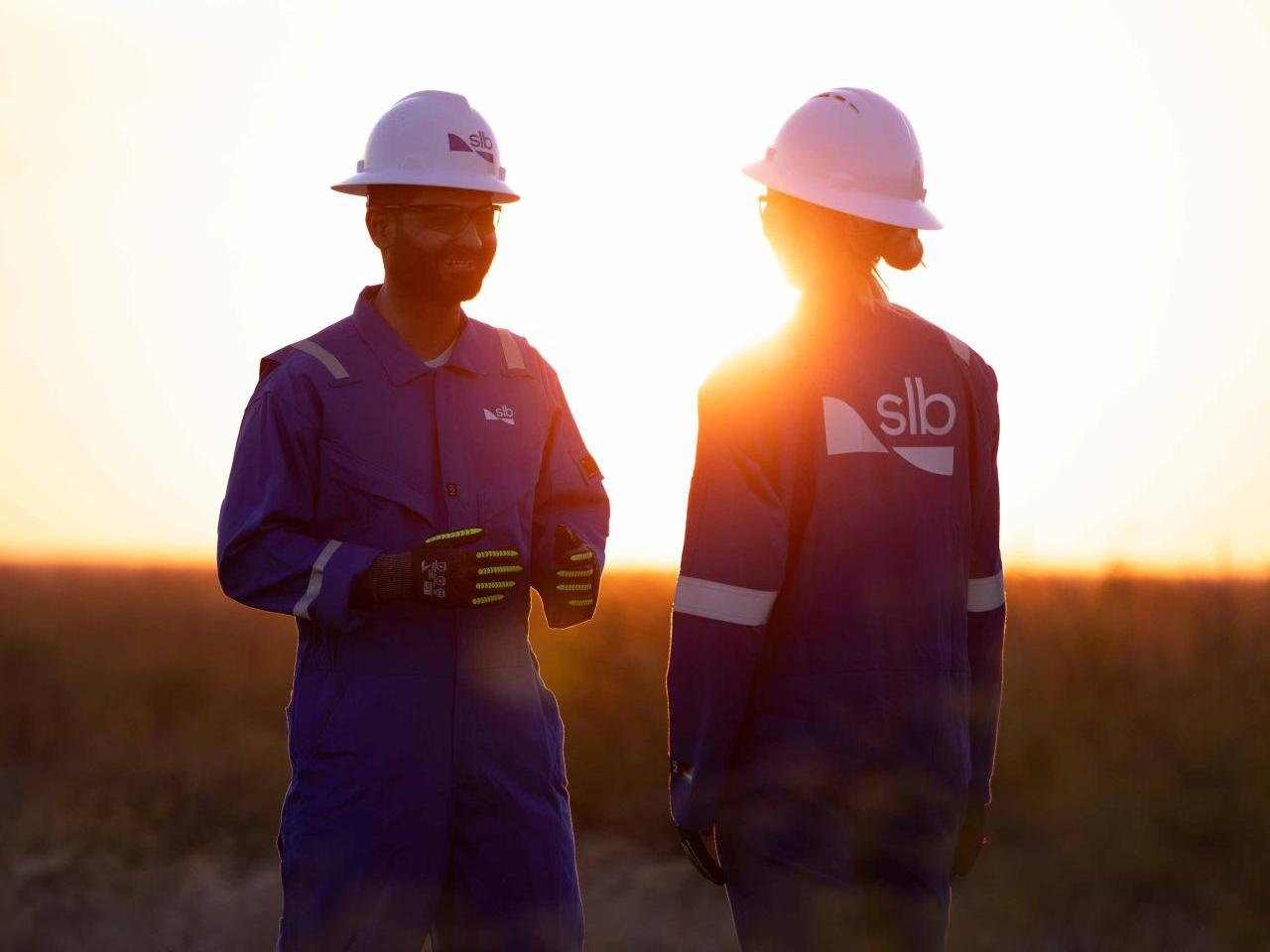 Two SLB workers talking with the sun setting behind them