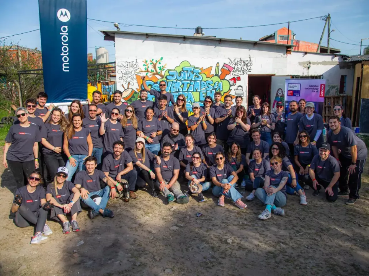 A group of volunteers posed outside a small building. Motorola sign to the side.