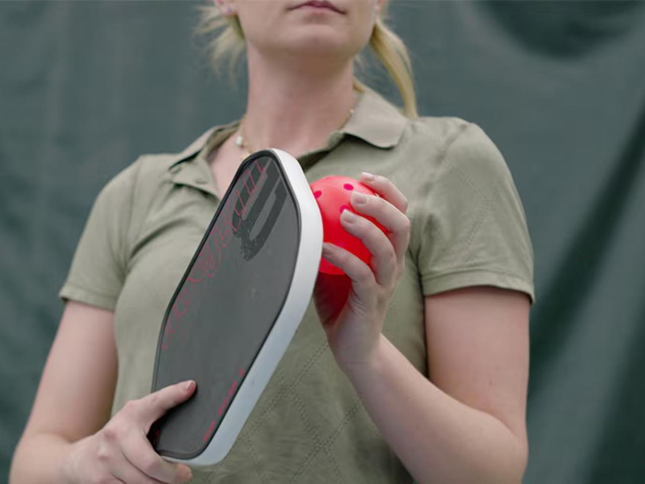 A person holding a pickleball racket and ball