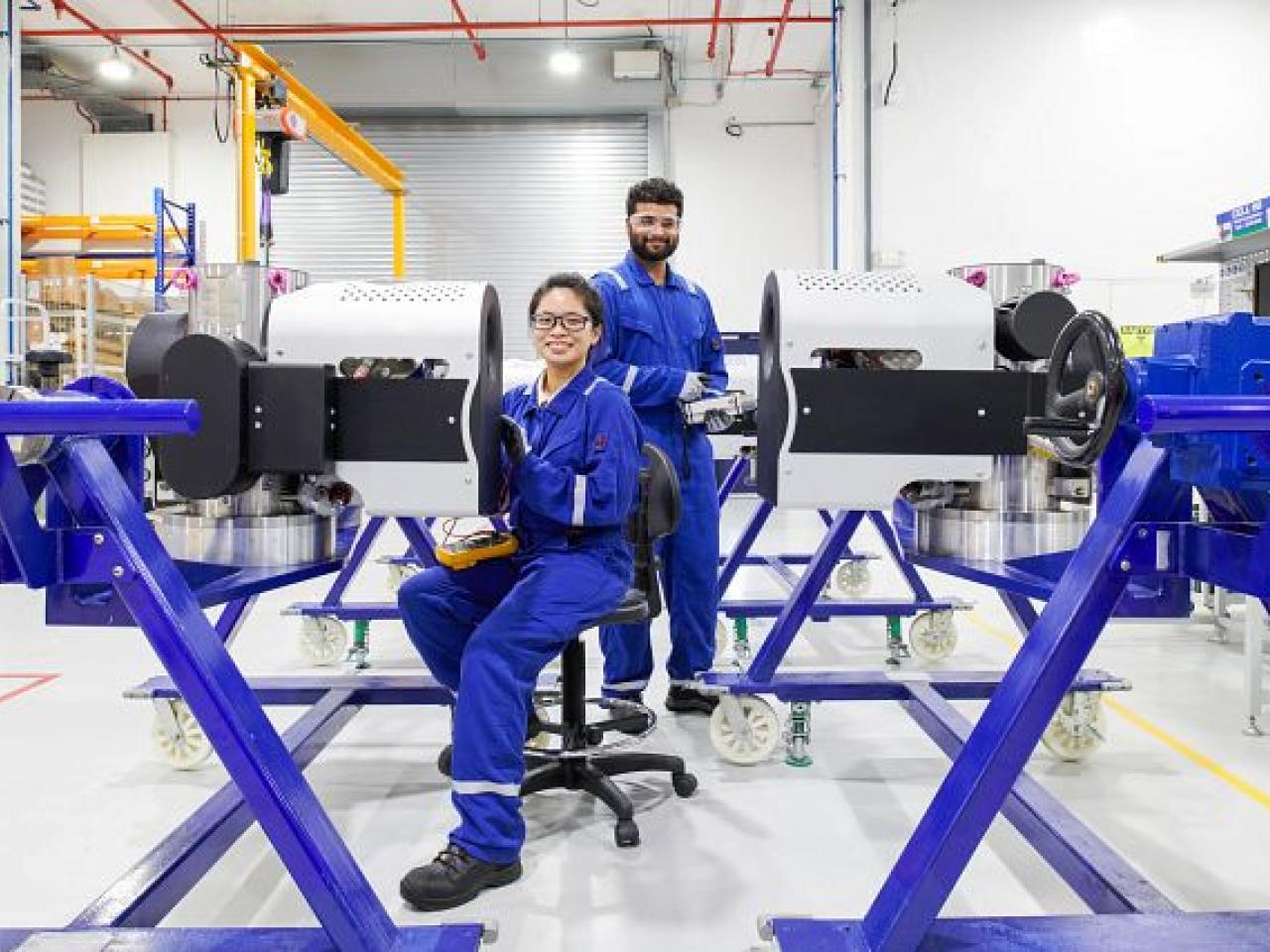 Two employees smiling at the camera. Each working on a piece of equipment