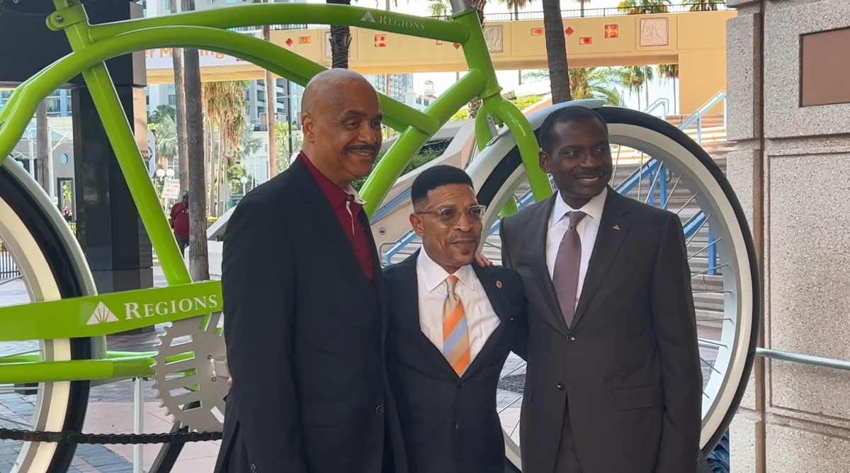 David Christian and two others with an arm around each other in front of a huge green bike.