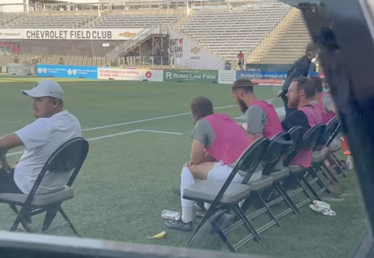 Soccer pitch with people wearing pink vests while sat on foldable chairs
