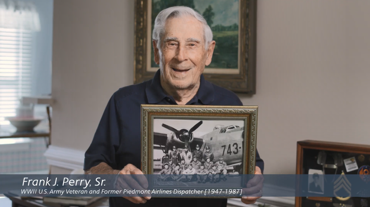 Frank Perry Sr. holding a picture of him and others in uniform by a plane.