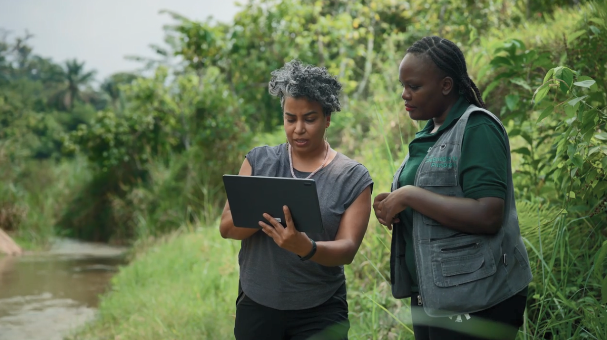 Two people looking at a laptop on a river bank.