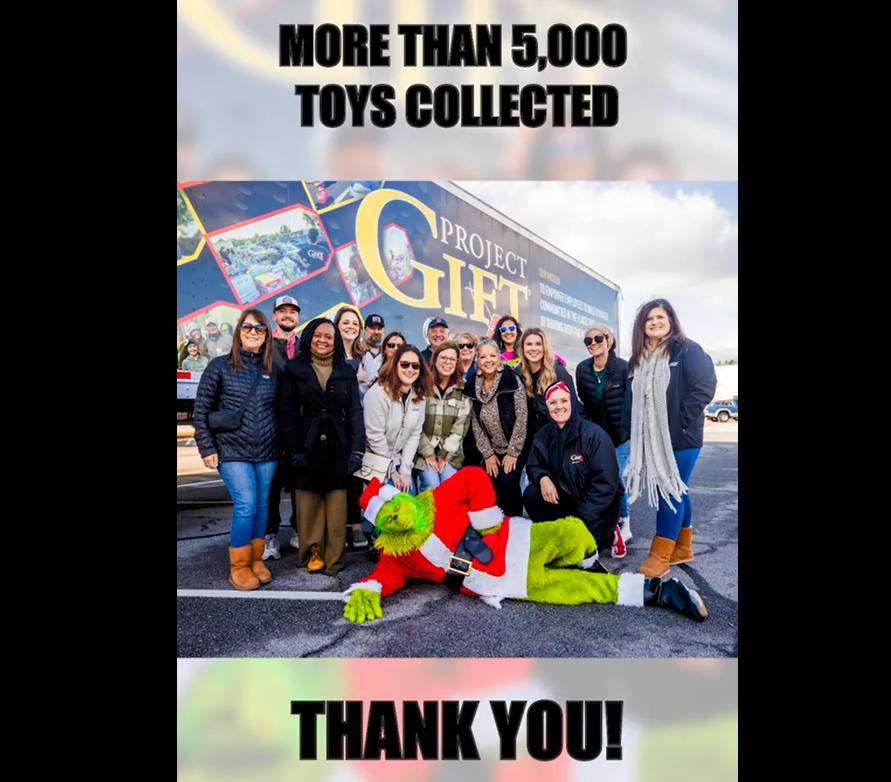 A group posed in front of a semi truck. A person dressed as the Grinch laid out in front of them. "Over 5000 toys collected, Thank you!"