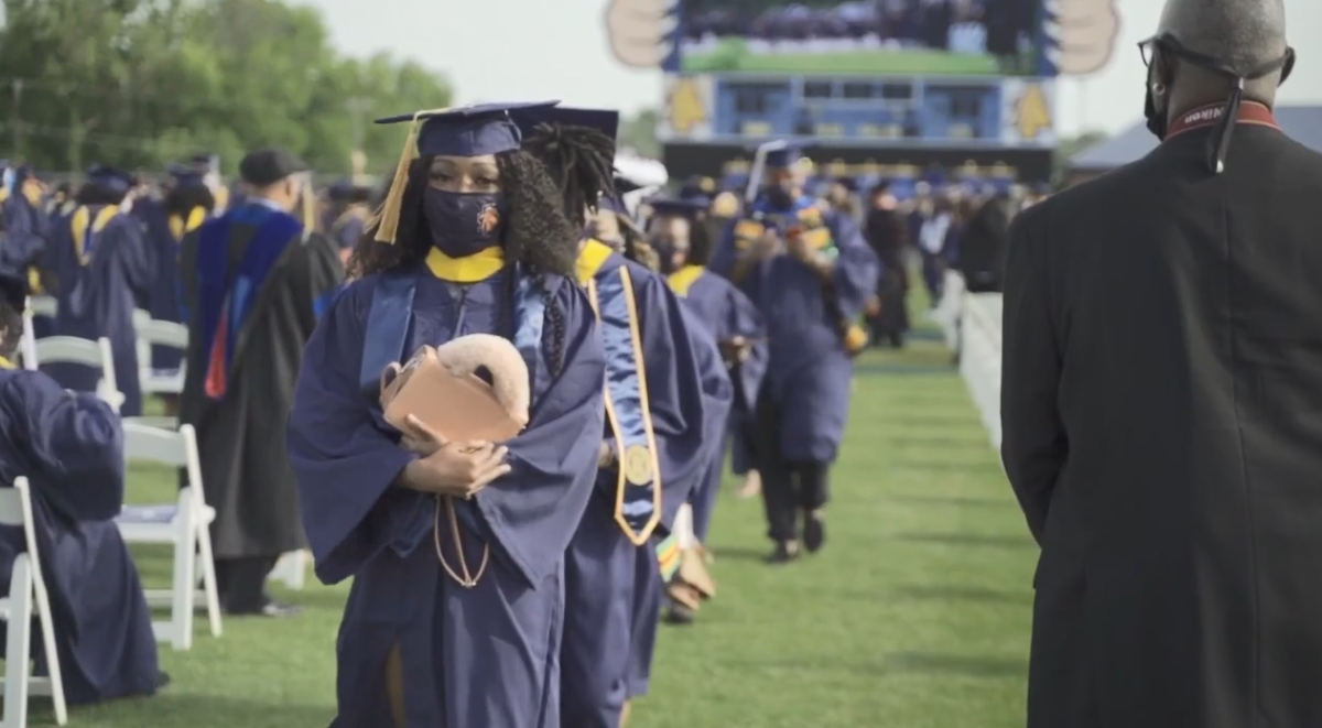 Outside, a line of graduates walking by rows of seated and standing audience members.