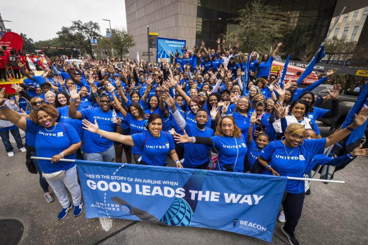 A large group of people wearing blue stand behind a blue parade banner with the words, "good leads the way" written in white