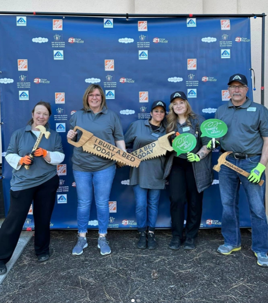 People posing with prop saws that read "I BUILT A BED TODAY"