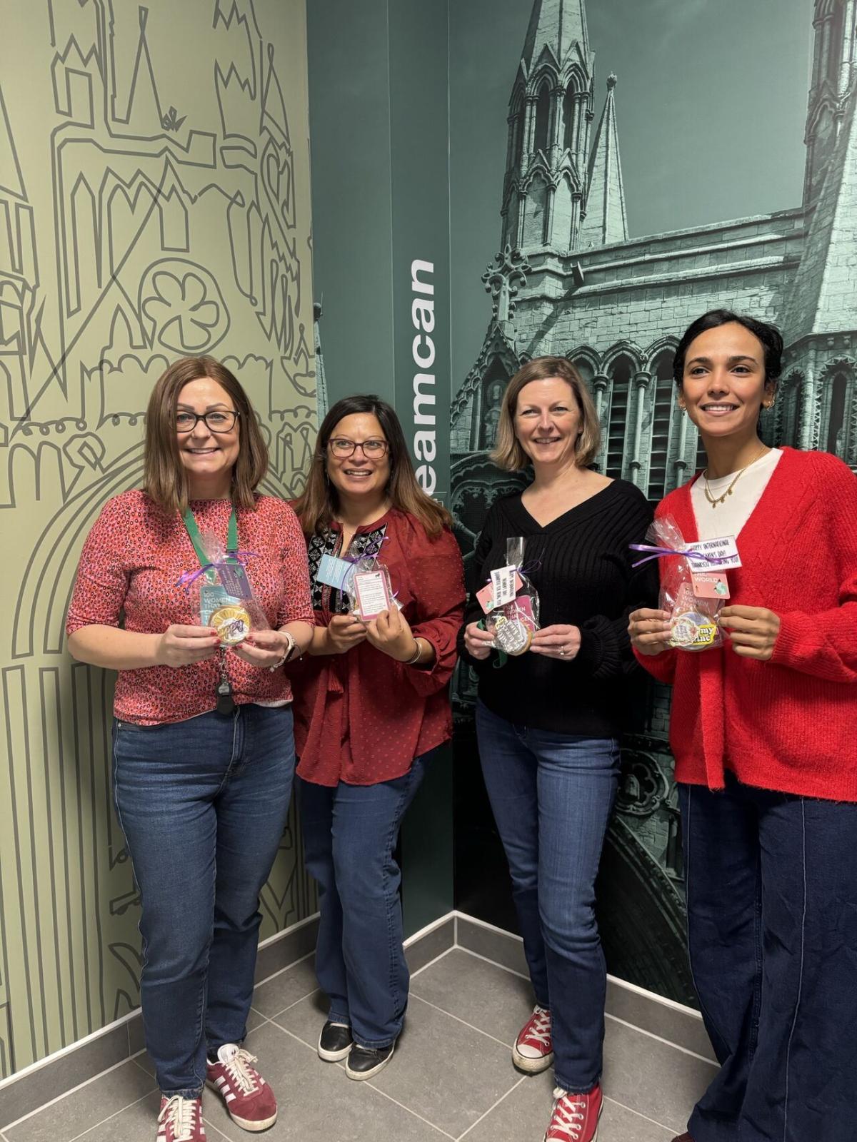 Four women stood next to each other holding a cookie