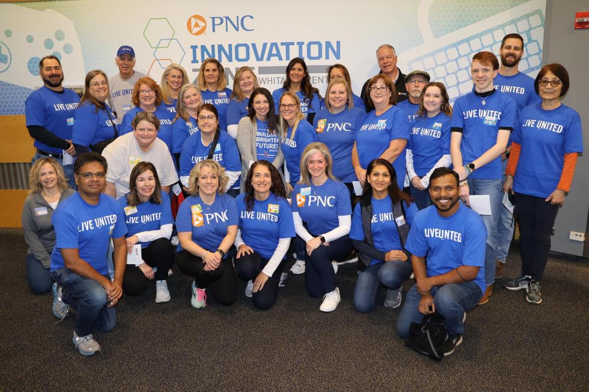 A group of people in blue t-shirts posed in front of a wall: "PNC Innovation"