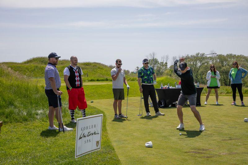 People standing on a green watching someone golfing