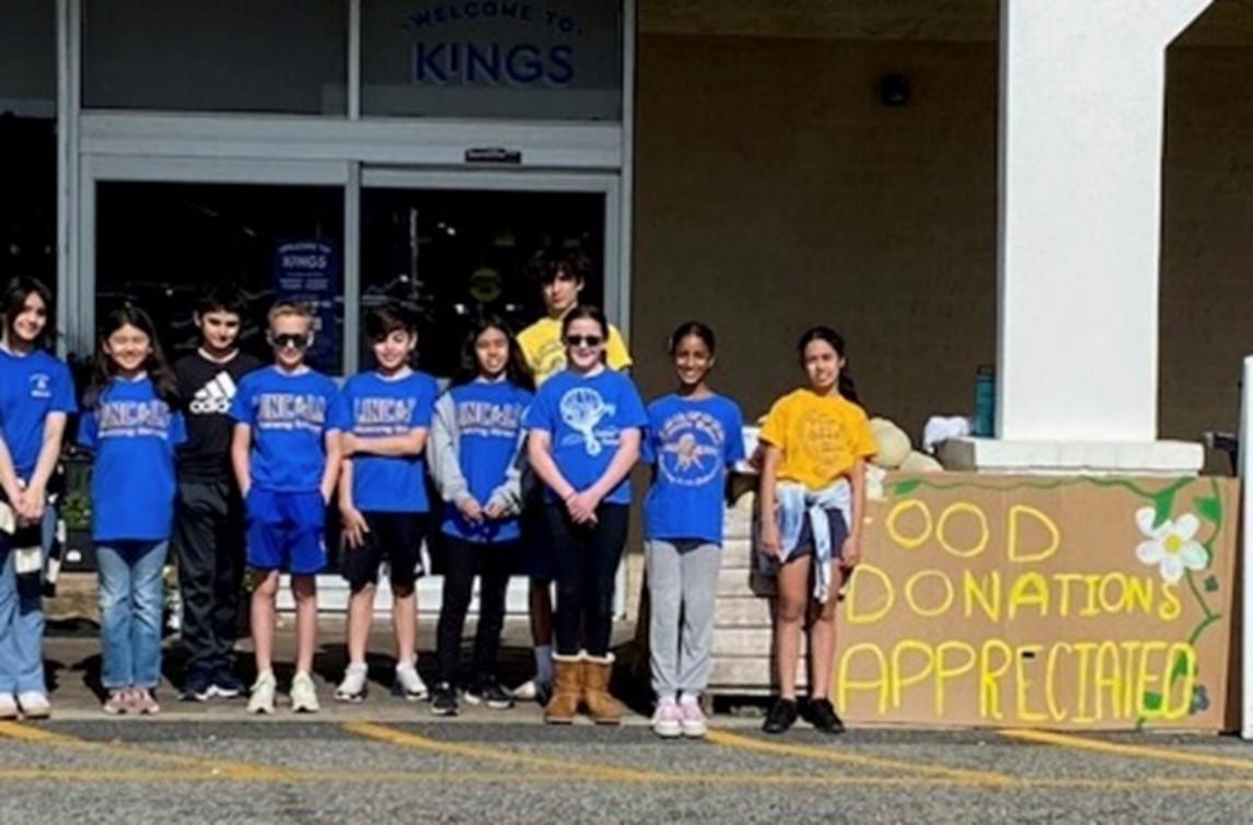 A group of people standing in front of a building with sign that reads "Food Donations Appreciated"