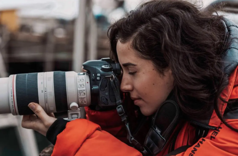 Brunette woman in orange jacket holding a camera