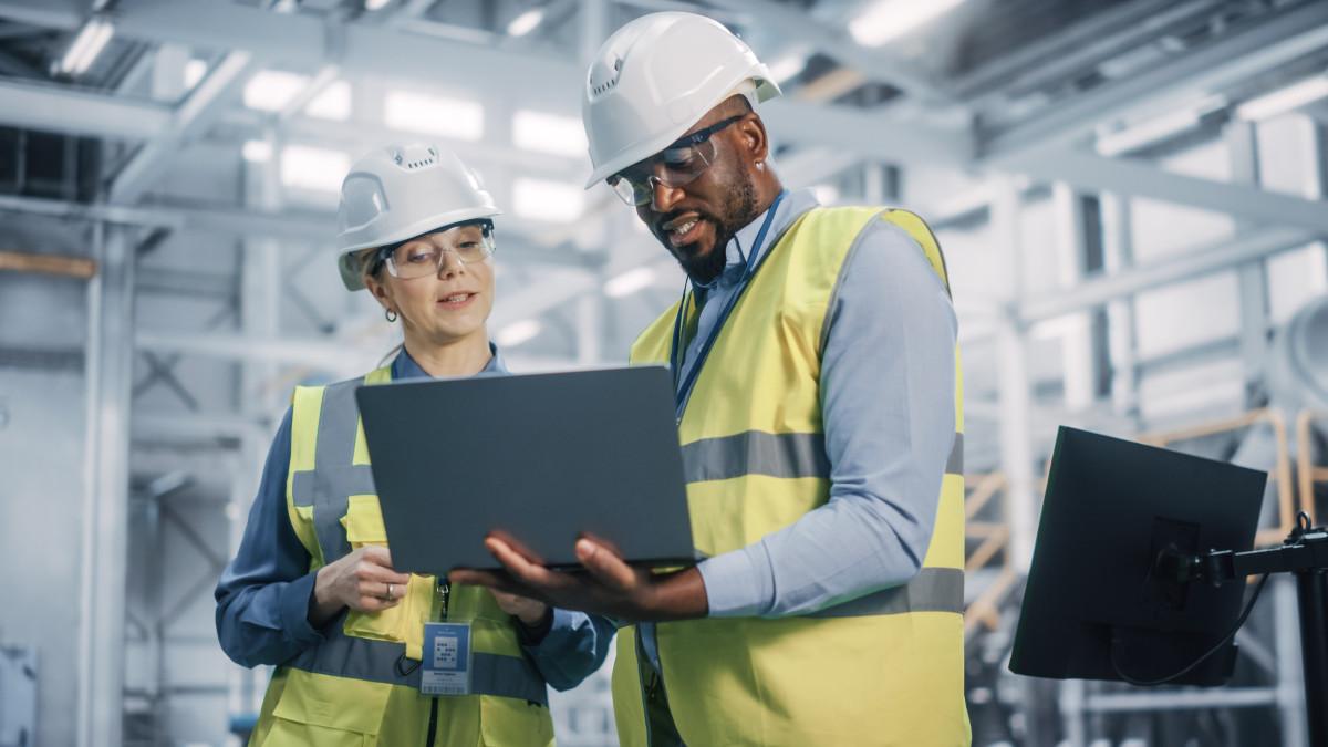 Workers in hard hats and safety vests looking at a laptop